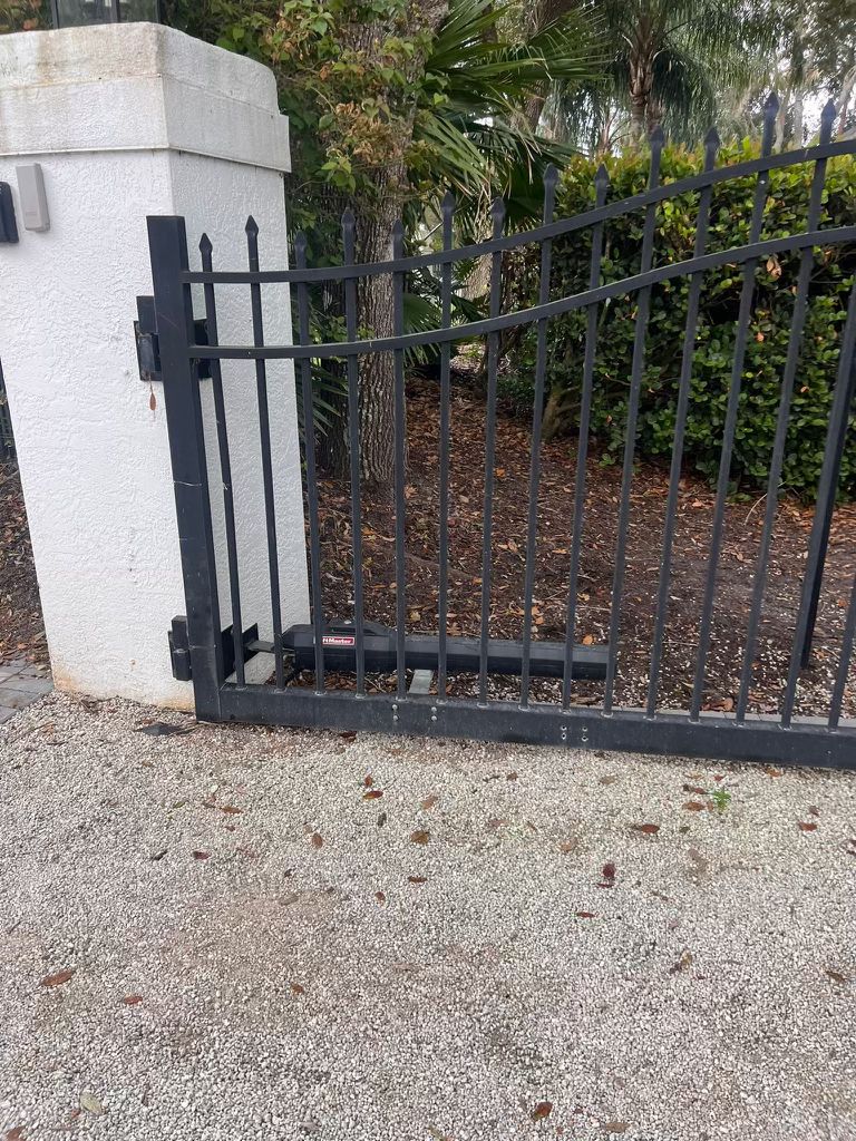 Automatic black metal driveway gate with opener on white pillar.
