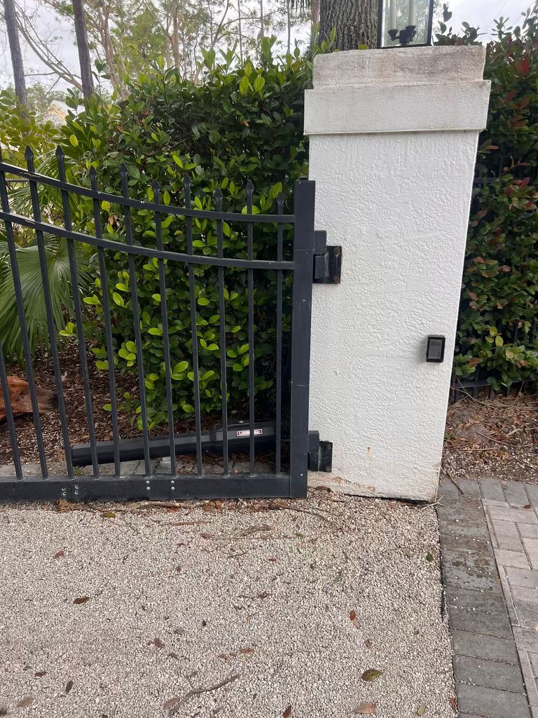 Black metal gate with opener attached to a white pillar.
