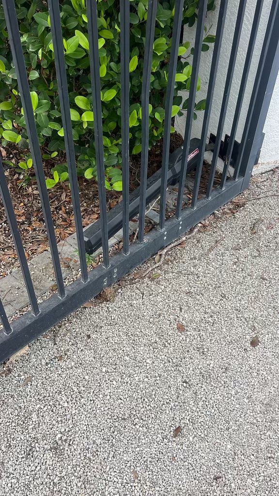 Black metal gate with green plants and a gate motor on gravel. in Mar Vista, CA